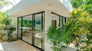 Uma casa moderna com um alpendre envidraçado, móveis de exterior e plantas tropicais.