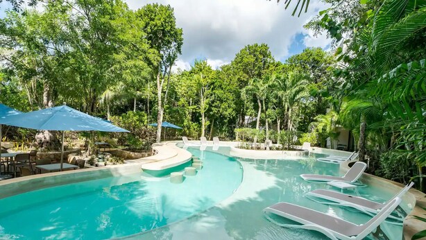 Piscina com espreguiçadeiras e guarda-sóis, cercada por vegetação exuberante.