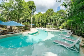 A swimming pool with lounge chairs and umbrellas, surrounded by lush greenery.