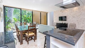 Uma cozinha moderna com uma ilha grande, uma sala de jantar com mesa de vidro e uma sala de estar com sofá.