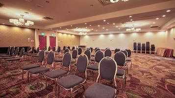 Un salón de conferencias con filas de sillas, piso alfombrado y una araña de cristal.