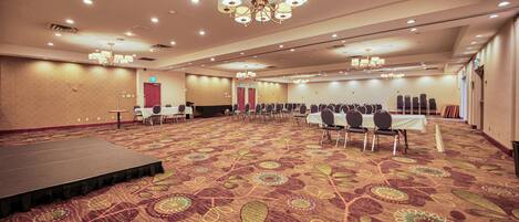 Un amplio salón de conferencias con un escenario, filas de sillas y una alfombra estampada.