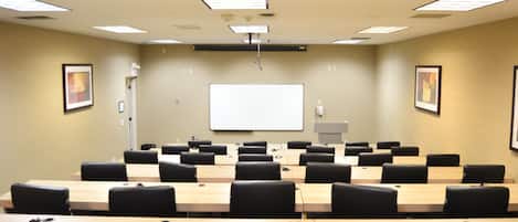 Un salón de conferencias con varias mesas y sillas, una pizarra y luces en el techo.
