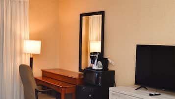 Habitación de hotel con escritorio, silla, televisor, cafetera y cómoda.