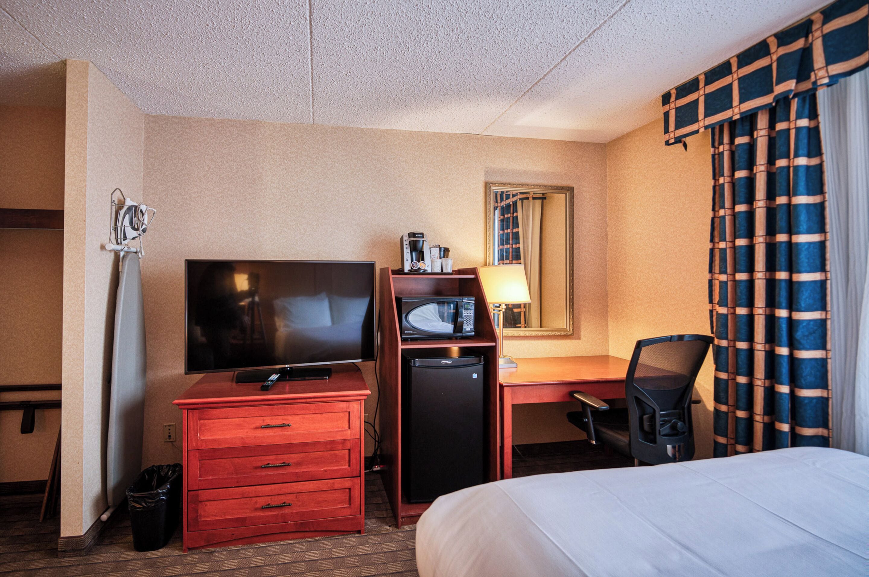 Habitación de hotel con cama, escritorio con computadora, televisión, microondas y bote de basura.