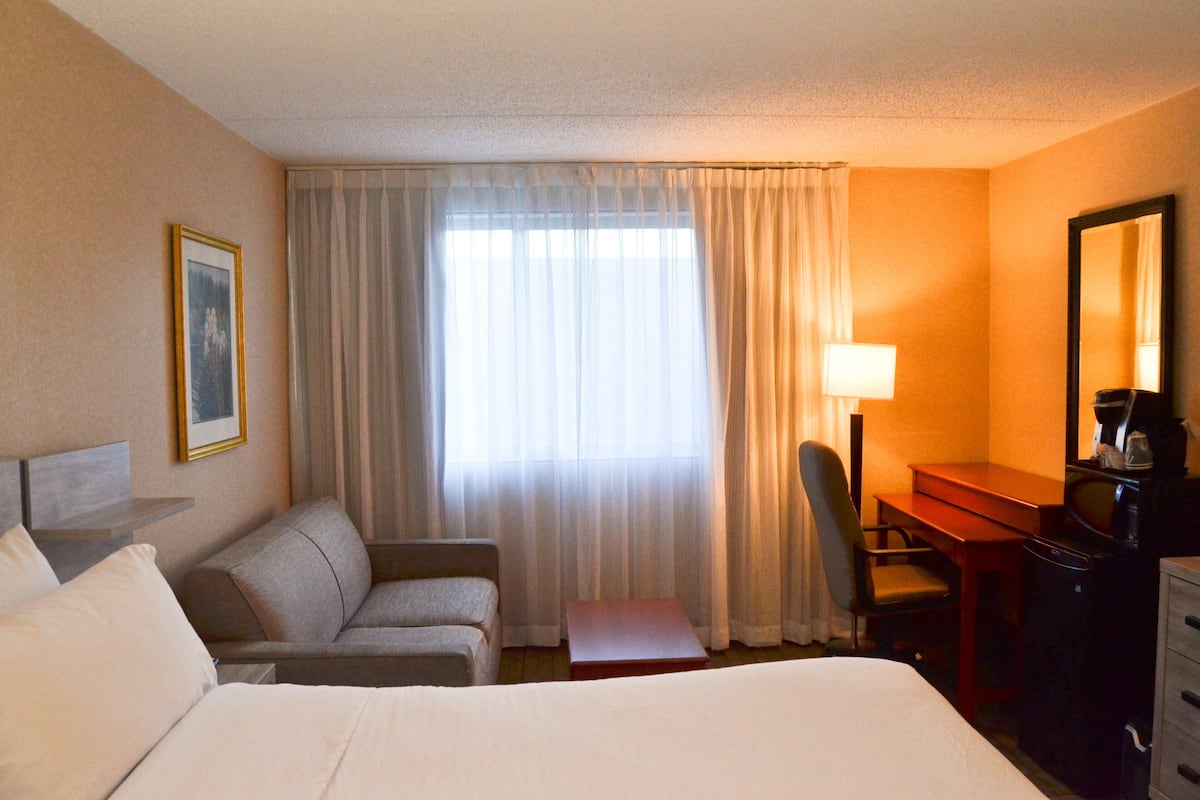 A hotel room with a bed, a desk, a chair, a lamp, and a window with curtains.