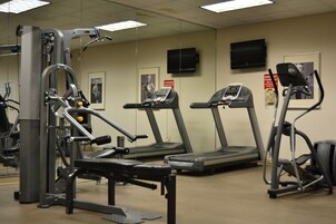 A gym with treadmills, a weight machine, and a television on the wall.