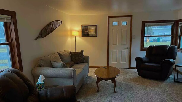 A living room with a sofa, armchair, and coffee table. There is a door and windows in the background. - Convenience in Kingsford

 (Kingsford)