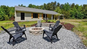 Una zona relax all'aperto con poltrone Adirondack e un braciere in pietra, circondata da un patio in ghiaia.