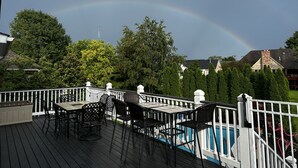 A deck with outdoor furniture, a swimming pool, and a rainbow in the background.