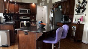 A modern kitchen with wooden cabinets, stainless steel appliances, a bar area, and a purple bar stool.