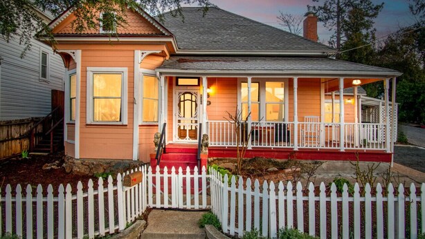 A two-story house with a porch, a white picket fence, and a red front door. - The Golden Parlor- Historic Victorian, Hot Tub (Grass Valley)