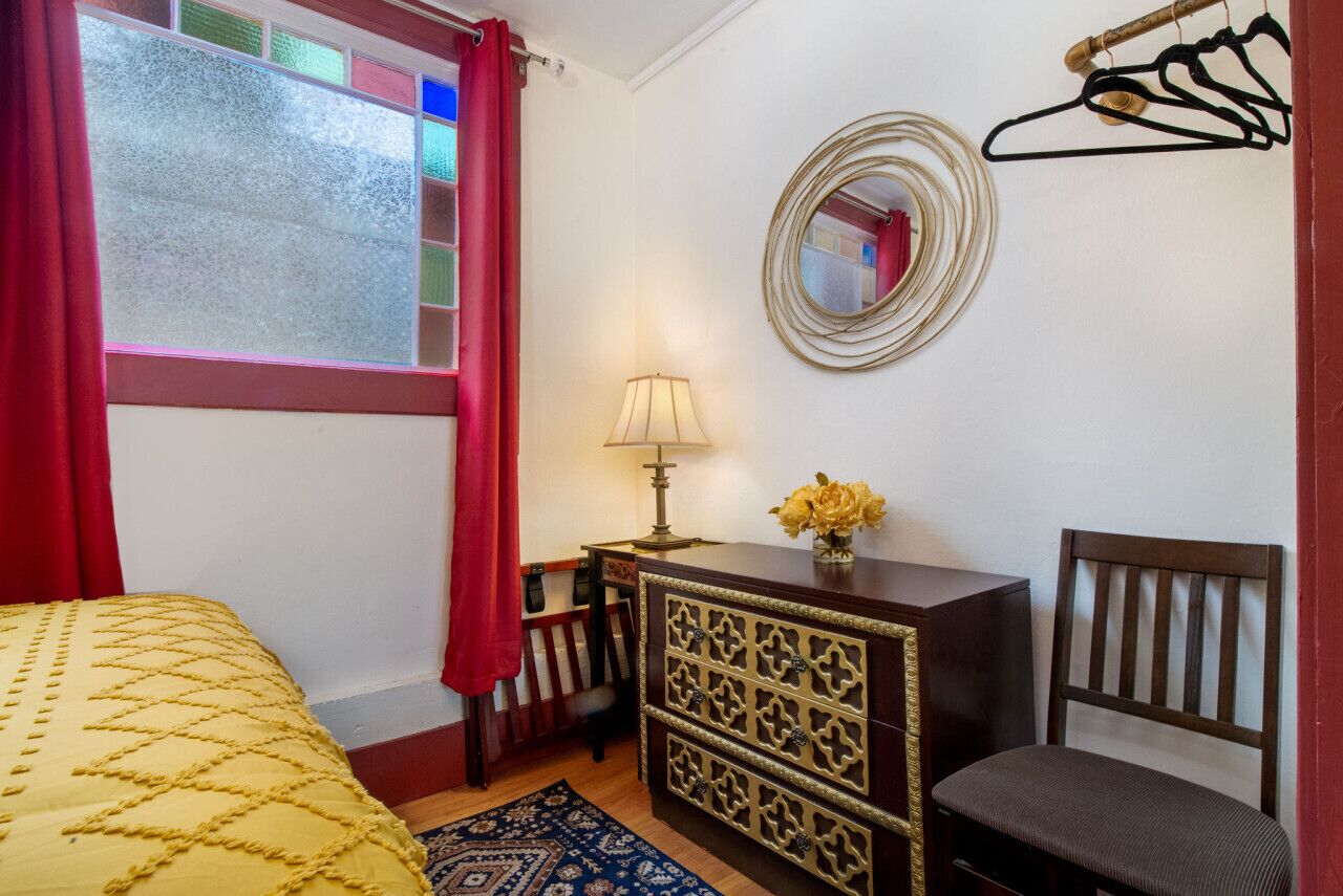A bedroom with a bed, a dresser, a chair, a mirror, and a window with curtains.