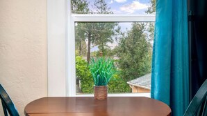Ein runder Holztisch mit einem gewebten Blumentopf in der Mitte, platziert neben einem Fenster mit Blick auf Bäume und ein Gebäude.