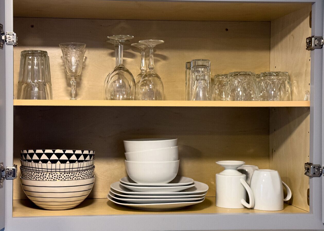 A wooden cabinet with shelves containing glassware, bowls, plates, and mugs.