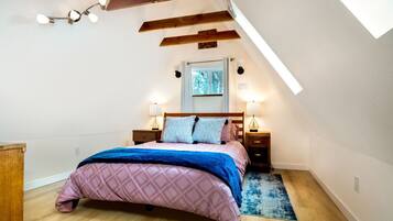 Une chambre avec un plafond en pente, un lit recouvert d’une courtepointe rose matelassée, deux lampes de chevet et une tête de lit en bois.