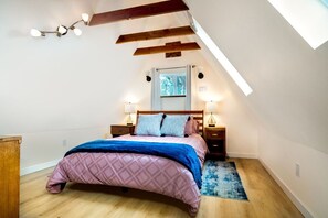 Un dormitorio con techo inclinado, una cama con colcha acolchada rosa, dos lámparas de noche y un cabecero de madera.