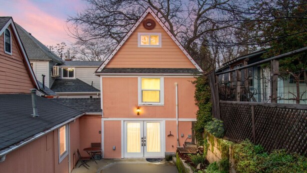 Ein zweistöckiges Haus mit einem Eingang in der Mitte, einer kleinen Terrasse und einem Holzzaun.