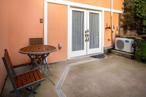 Un patio con una mesa redonda y dos sillas, una puerta corrediza de vidrio y una unidad de aire acondicionado.