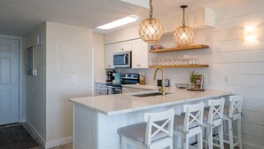 Una cocina moderna con una isla central, armarios blancos e iluminación colgante.