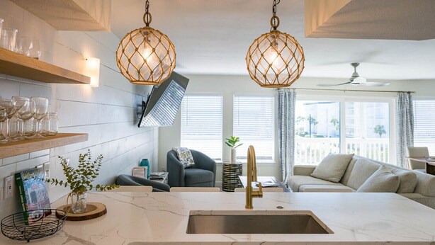 Una cocina moderna con una isla central, luces colgantes y vistas a una sala de estar.
