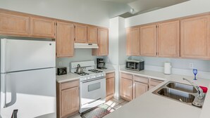 A kitchen with wooden cabinets, a white refrigerator, a stove, a microwave, and a sink. - Victorville Home w/ Fenced Backyard + Patio! (Victorville)