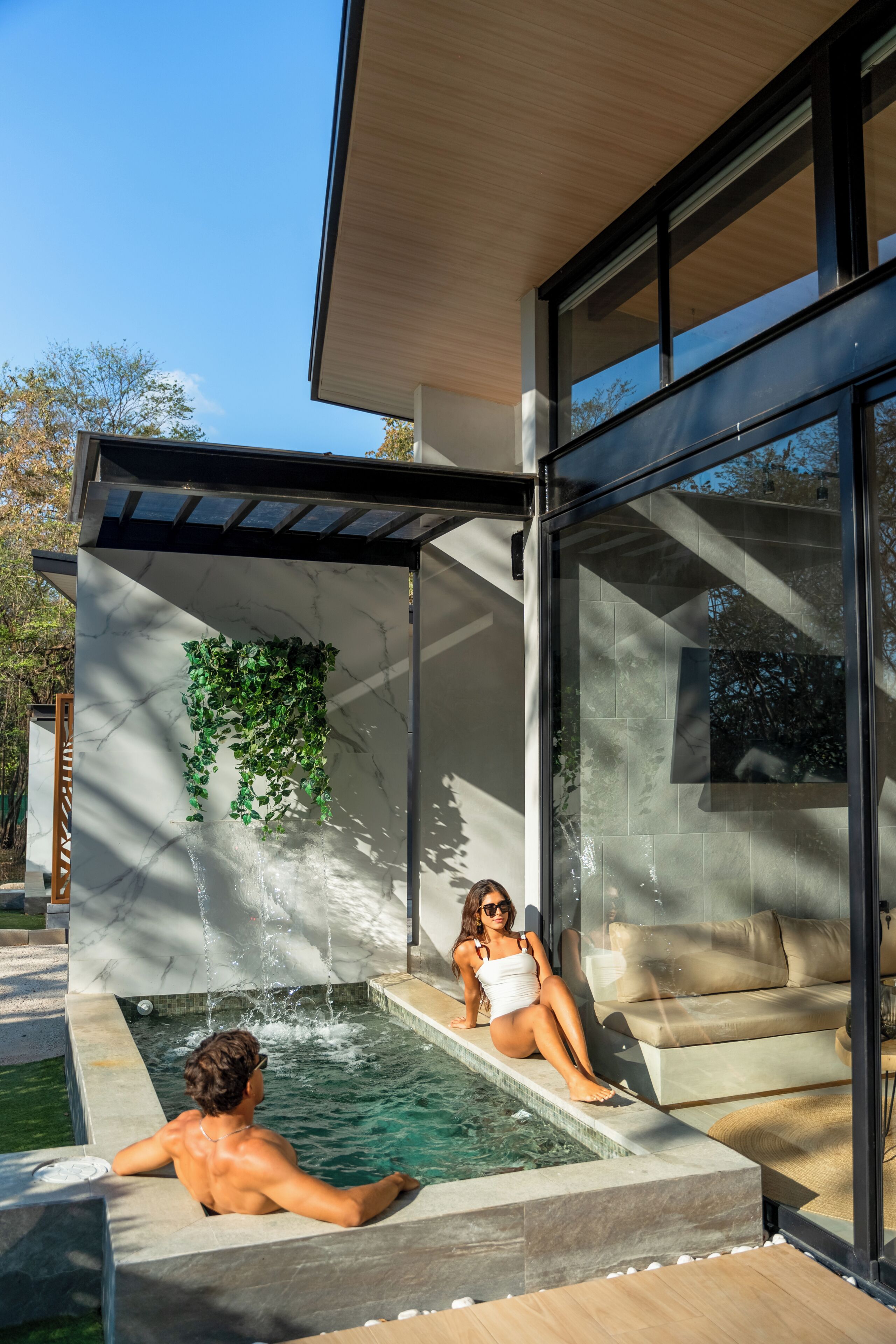 A modern outdoor pool area with a glass enclosure, a built-in seating area, and a water feature.
