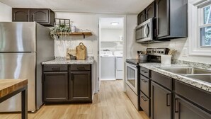 A modern kitchen with dark cabinetry, stainless steel appliances, and a marble countertop. - The Farmer's Cottage at Kings Crossing (Fredericksburg)