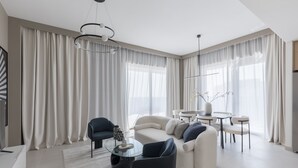 A modern living room with a sectional sofa, a glass coffee table, and a dining area with a round table and chairs. - Creek Beach Roomy 3BR with terrace (Dubai)