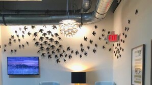 A modern office space with two grey armchairs, a round table with a plant, a wall-mounted TV, and a decorative light fixture. - Designed Living in Rochester's Only ApartHotel (Rochester)