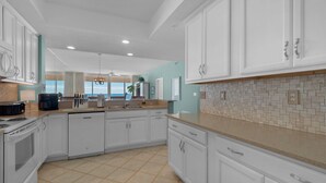 A modern kitchen with white cabinets, a tiled backsplash, and a view to the outside. - Relax in 409...Get in a Flip-Flop State of Mind (Navarre)