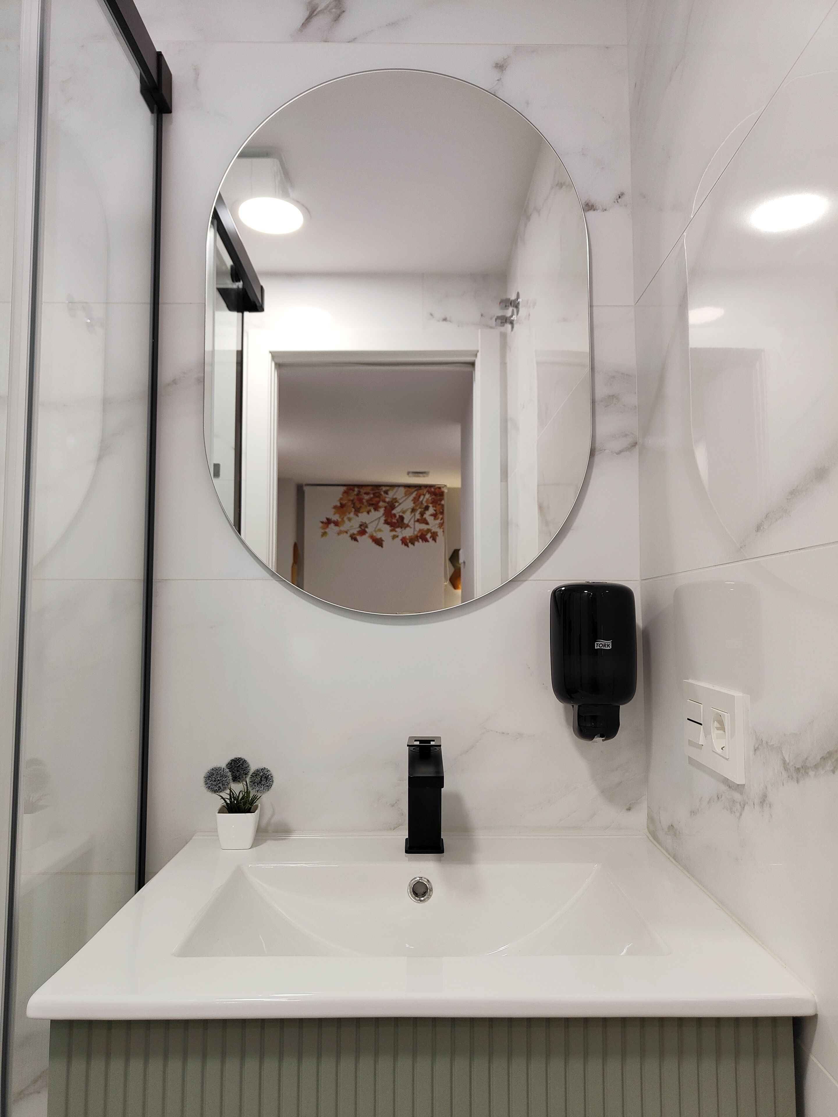 A bathroom with a white sink, a round mirror, and a TORK soap dispenser.