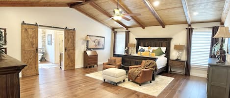 A spacious bedroom with a large bed, wooden ceiling beams, and a sliding barn door.