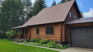 A log cabin with a metal roof, a porch, and a garage. - Adventure Cabin -Coolin Priest Lake; king bed, bunks, ATV and snowmobile parking (Coolin)