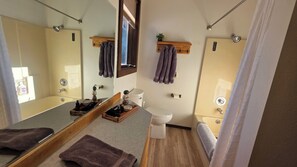 Une petite salle de bain comprenant des toilettes, un lavabo et un miroir. Des serviettes et des articles de toilette sont posés sur le comptoir.