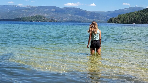 A person standing in clear water with mountains in the background. - Adventure Cabin -Coolin Priest Lake; king bed, bunks, ATV and snowmobile parking (Coolin)