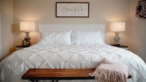 A neatly made bed with a white quilt, two bedside lamps, a framed quote on the wall, and a bench with a fringe throw blanket. - Luxury on Seneca Wine Trail, 3 King Beds with Awesome Country View (Watkins Glen)