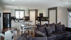 A modern kitchen with a central island, a dining area with a white table and chairs, and a dark grey sofa in a living room area. - Luxury on Seneca Wine Trail, 3 King Beds with Awesome Country View (Watkins Glen)