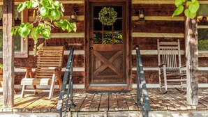 A wooden cabin with a large door, a porch with a bench, and a rocking chair. - The Cabin at Roney Creek Ranch (Cottontown)