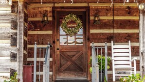 A wooden cabin with a wooden door, a welcome wreath, and two white chairs outside. - The Cabin at Roney Creek Ranch (Cottontown)