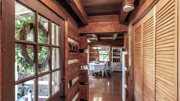 A wooden interior with a dining area, wooden shutters, and a view through a window with a wreath. - The Cabin at Roney Creek Ranch (Cottontown)