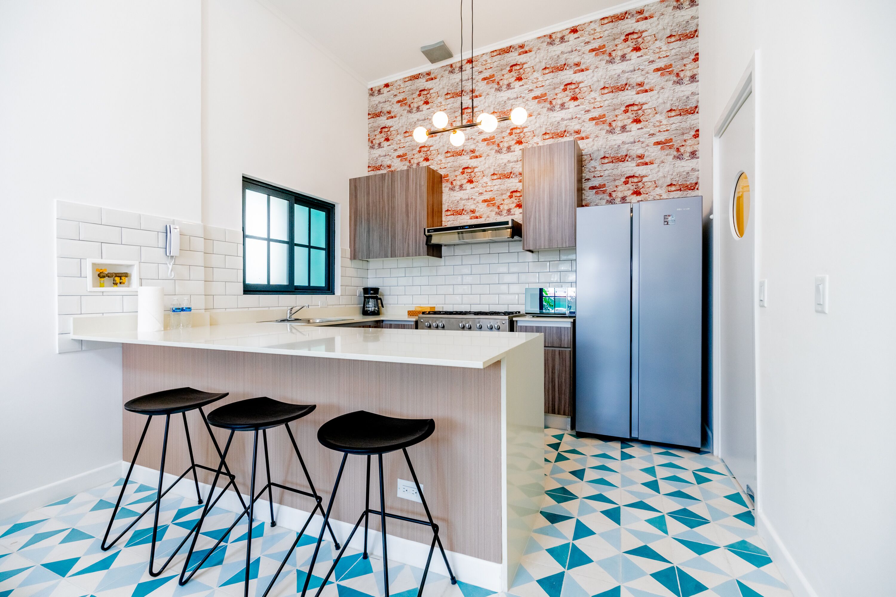 A modern kitchen with a central island, bar stools, a refrigerator, and a patterned backsplash.