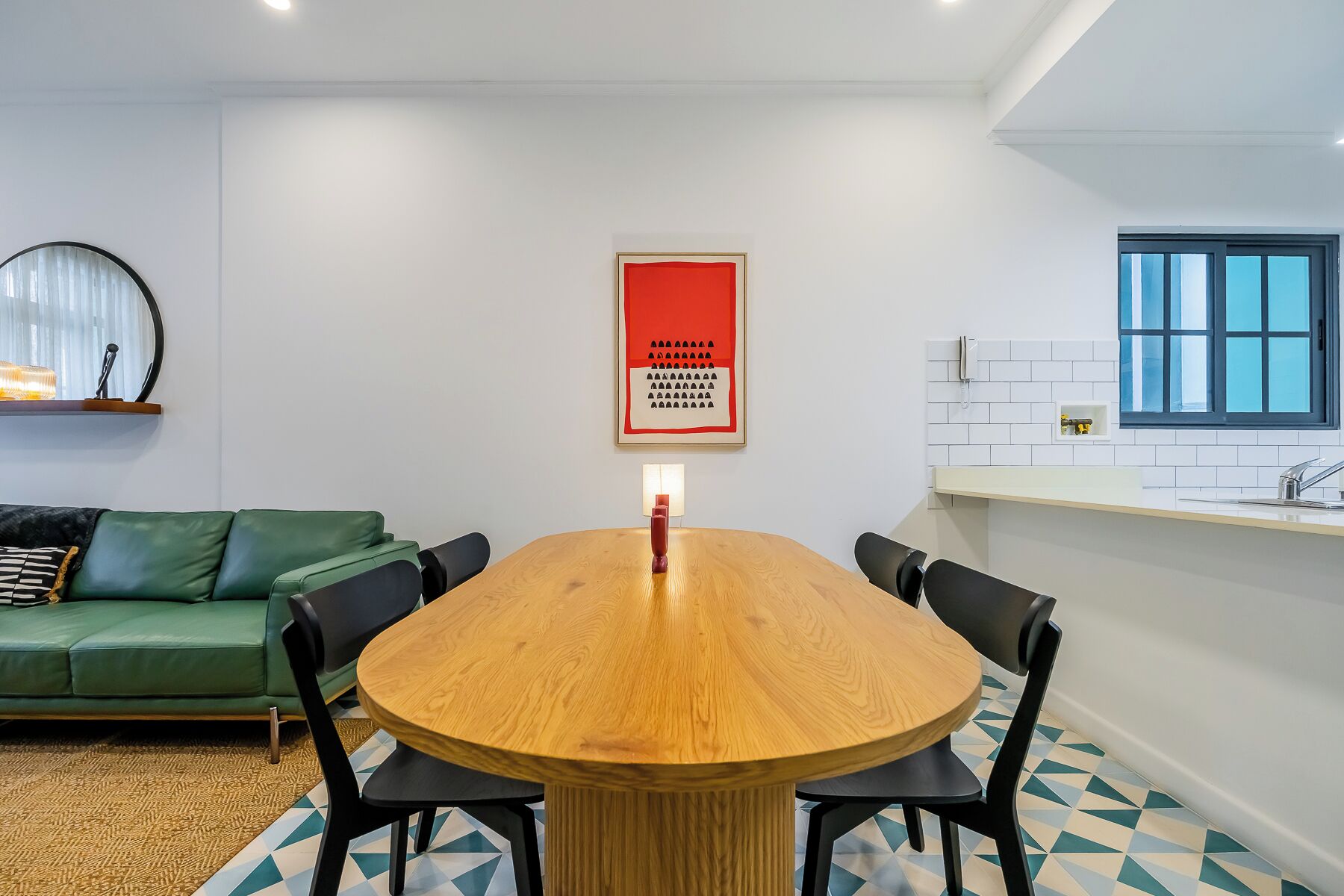 Un espace de repas moderne avec une table en bois, des chaises noires, un canapé vert et un sol à motifs géométriques.
