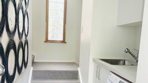 Un lavadero con lavadora, lavabo y ventana con persianas.