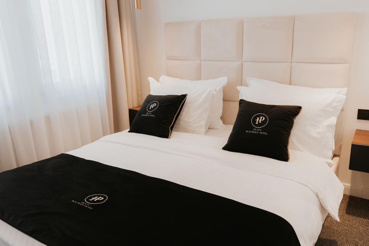 A hotel room with a large bed, white bedding, and black pillows with a logo.