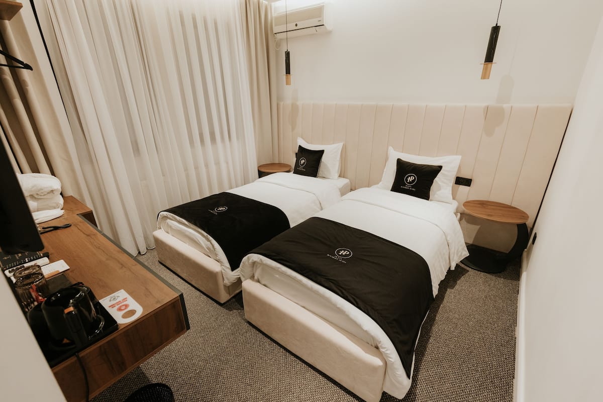 A hotel room with two beds, a desk with a coffee maker, a small round table, and a hanging light fixture.