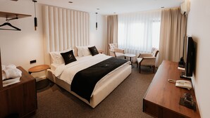 A hotel room with a large bed, a desk, a chair, a TV, and a bedside table with a lamp.