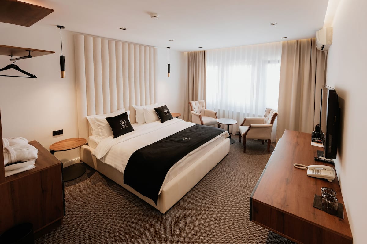 A hotel room with a large bed, a desk, a chair, a TV, and a bedside table with a lamp.