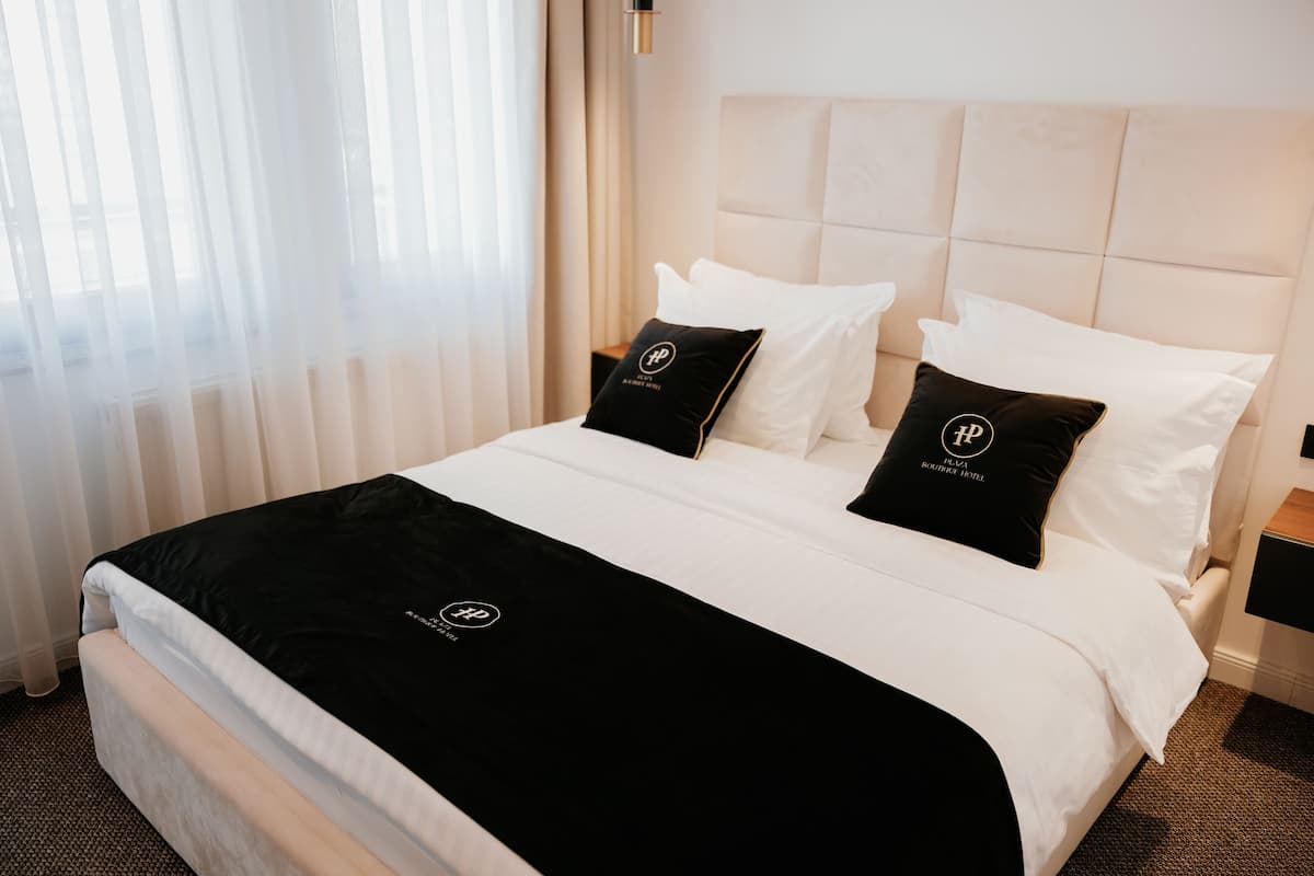 A hotel room with a large bed, white bedding, black and white pillows, and a black throw blanket.