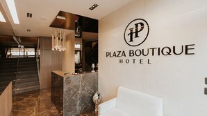 A modern hotel lobby with a marble reception desk, a white sofa, and a staircase leading to upper floors.